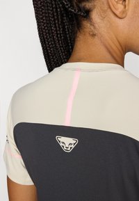Grå og beige træningsskjorte med en pink detalje, glat tekstur og et logo på ryggen, der illustrerer et moderne og sporty design.