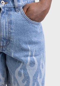 Mano appoggiata all'interno della tasca anteriore di un paio di jeans di denim blu con leggere macchie chiare sulla coscia.