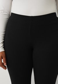 Sorte leggings i et glat og strækbart stof med en elastisk talje, der har et enkelt design uden mønstre eller dekorationer.