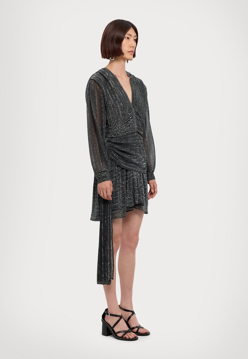 Black metallic mini dress with long sleeves, ruched waist, and a flowy skirt. Paired with black strappy block-heel sandals.