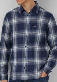 Blauw-wit geruit flanellen overhemd met lange mouwen, knopen aan de voorkant, borstzak en zwarte knopen. Zachte textuur met een ontspannen pasvorm.