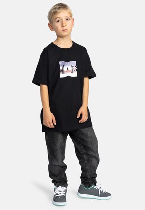 Černé tričko s grafickým logem, spárované s tmavě šedými džíny a šedými teniskami s tyrkysovými akcenty. Jednoduchý, neformální streetwear styl.