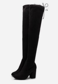 Botas de ante negras por encima de la rodilla con tacones altos en bloque y cintas ajustables en la parte posterior superior.