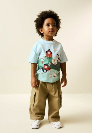 Light blue cotton t-shirt with colorful farm-themed embroidery, paired with beige cargo pants and white sneakers. Short sleeves and relaxed fit.