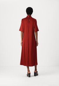 Vestido color óxido hecho de tela suave, con mangas cortas, un alto cuello y un detalle de ojal en la espalda. Diseño hasta el suelo.