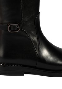Schwarze Leder-Stiefel bis zum Knie mit glatter Oberfläche, ausgestattet mit einem Seitenriemen mit einer metallischen Schnalle und Nietenakzenten an der Ferse.