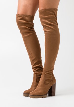 Brązowe zamszowe kozaki za kolano z masywnym obcasem i żebrowaną podeszwą. Gładka faktura i dopasowany krój podkreślają długość nóg.
