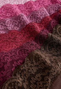 Bandes de tissu en dentelle empilées dans des tons roses, violets, rouges et bruns avec motifs floraux et bordures festonnées.