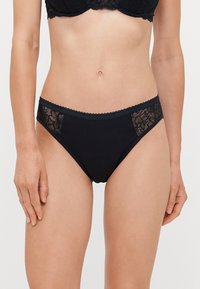 Czarne figi bikini z kwiecistymi koronkowymi panelami po bokach, gładkim głównym materiałem i falbaniastym wykończeniem wzdłuż pasa.