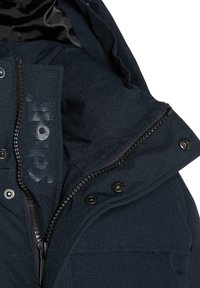 Chaqueta azul oscuro con cierre de cremallera y acentos de botones. Tejido suave con un forro interior suave, que presenta una etiqueta de logo en la zona del cuello.