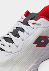 Λευκό αθλητικό παπούτσι με γκρι και κόκκινες λεπτομέρειες, λευκά κορδόνια και υφασμάτινο επάνω μέρος με υφή και λογότυπο στη πλευρά.