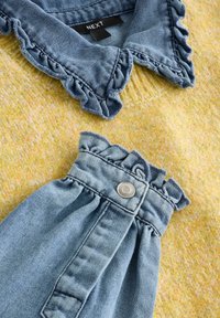 Tissu texturé jaune clair avec un col en denim aux bords froncés. La partie inférieure en denim a une taille froncée et un détail de bouton.