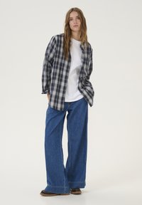 Geruite, marineblauwe en witte flanellen shirt over een wit t-shirt; gecombineerd met oversized blauwe denim broek en zwarte schoenen met een gestructureerde zool.