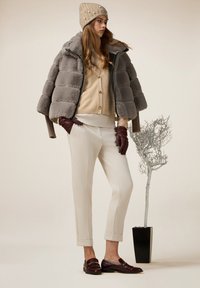 Giacca imbottita grigia sopra un maglione crema, un cardigan beige, pantaloni crema e mocassini bordeaux. Berretto beige con decorazioni. Decorazione minimalista.