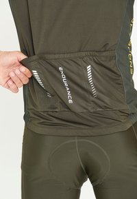 T-shirt de sport vert foncé avec une finition texturée, doté d'une poche arrière étiquetée "ENDURANCE" et bordée de bandes réfléchissantes.