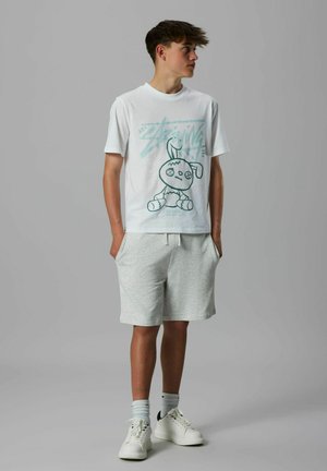 T-shirt en coton blanc avec un imprimé graphique d'un lapin en teal. Associé à un short en polaire gris clair et des baskets blanches avec des accents noirs.