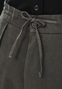 Szare bawełniane spodnie dresowe ze sznurkiem, o teksturowanej powierzchni; mają wiązany sznurek i metalowe oczko. Czarny guzik widoczny powyżej pasa.