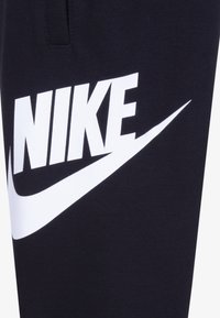 Nike trenerke u tamnoplavoj boji s velikim bijelim logotipom i dizajnom swoosh. Izrađene od mekanog materijala, s elastičnom trakom u struku i džepom.