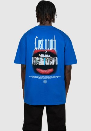 Blå bomulds T-shirt med fed hvid tekst "Lost youth" og et grafisk motiv af røde læber, der holder på sedler, med en slogan nedenfor.