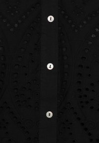 Black fabric button-up shirt featuring intricate cut-out embroidery patterns, with round, silver buttons along the front.