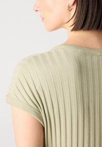 Ribbed, oliivivihreä pusero, jossa on lyhyet hihat. Sujuva pinta ja pyöreä kaula-aukko, hienovaraiset pystysuorat raidat ja muotoiltu malli.