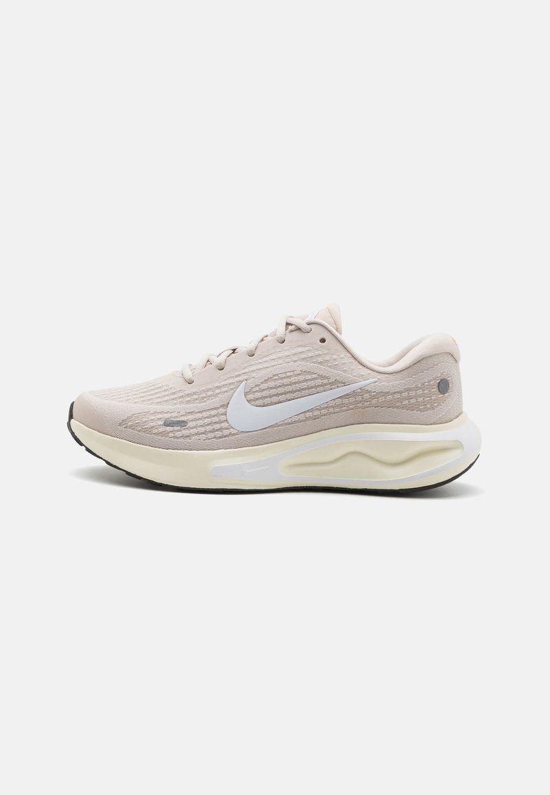 Sapatilha atlética bege claro com um upper texturizado, logótipo swoosh branco, sola flexível e detalhes subtis. Projetada para conforto e desempenho.
