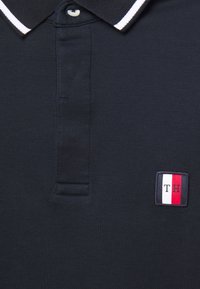 Polo bleu marine en coton avec une finition texturée, doté d'un col à rayures blanches et d'un petit logo brodé en rouge, blanc et bleu.
