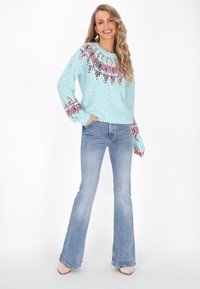 Maglione azzurro chiaro con dettagli a motivo in bordeaux e bianco, abbinato a jeans in denim svasati. Tessuto morbido e vestibilità rilassata.