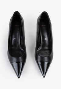 Tacchi alti in pelle nera con punta affusolata, finitura liscia e suola piatta. L'interno presenta testo impresso: "VERA PELLE." Design minimalista.