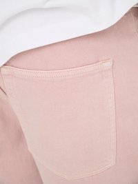 Gros plan sur un tissu en denim rose clair montrant une poche arrière cousue avec un vêtement blanc plié dessus.
