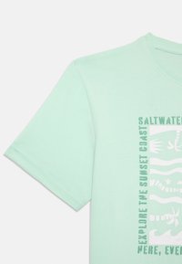 Miętowy bawełniany t-shirt z krótkimi rękawami, zdobiony graficznym nadrukiem z tekstem i wzorami w białym i ciemnozielonym kolorze.