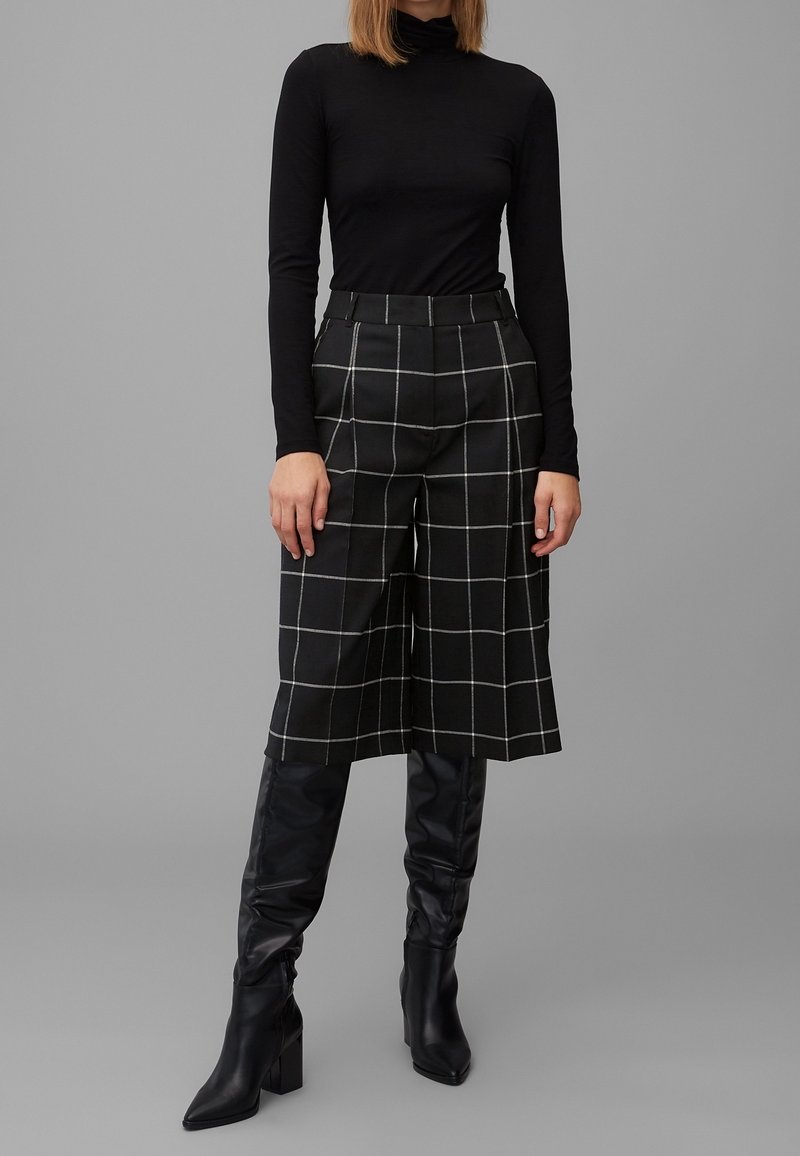 Col roulé noir à manches longues associé à un pantalon court taille haute à carreaux noirs et blancs, complété par des bottes noires élégantes montantes jusqu'aux genoux.
