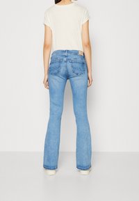 Ljusblå utsvängda jeans i denim med medelhög midja, som har två bakfickor och en tan läderetikett vid midjan.