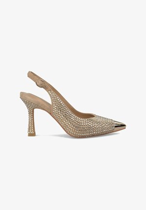 Zapatos de tacón alto beige con tiras traseras, adornados con pedrería, punta afilada y puntera metálica dorada. Tacón texturizado con base cuadrada.