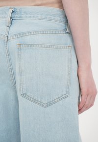 Világoskék farmernadrág magas derekkal, hátulján gyémánt alakú zsebbel és finom varrási részletekkel.