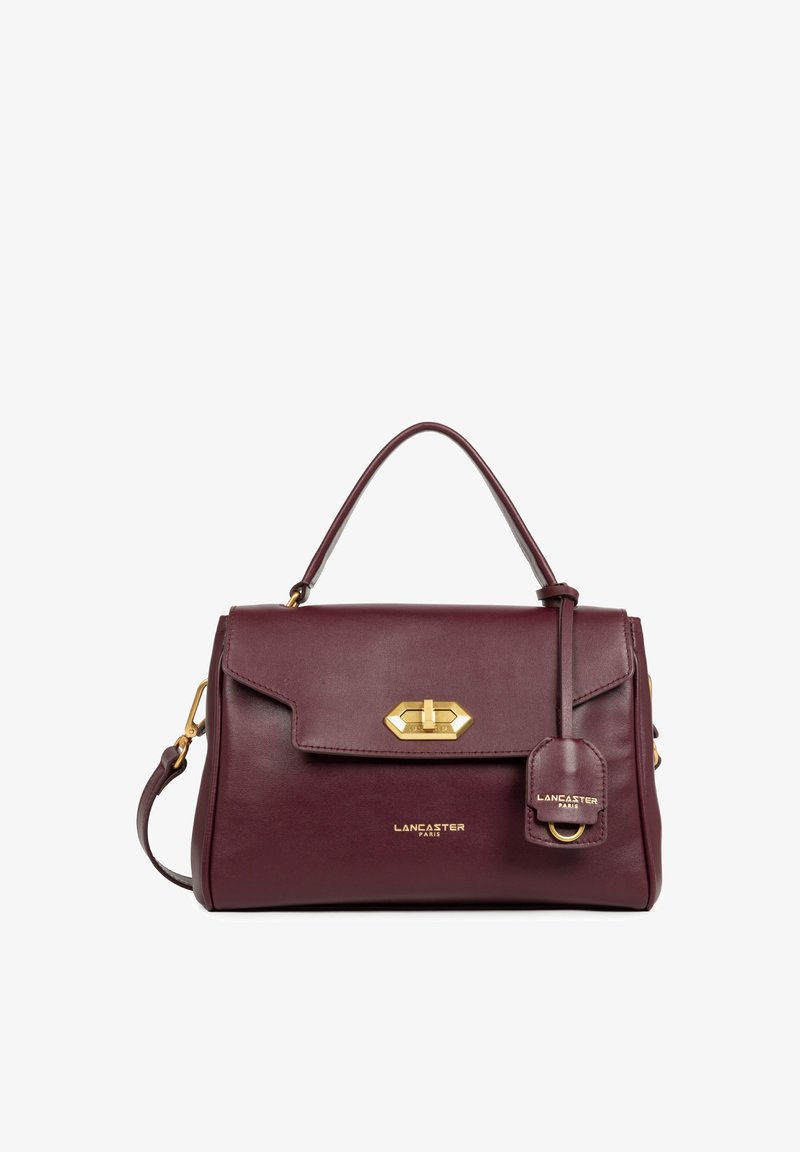 Sac à main en cuir bordeaux avec un design structuré, quincaillerie dorée, fermeture à rabat et une étiquette amovible arborant le logo.