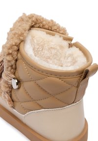 Botine bej cu o textură matlasată, căptușeală moale la interior și un accent tricotat creț în jurul gâtului. Au o talpă plată și accesorii metalice.