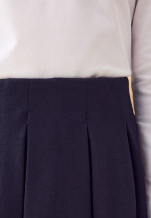 Granatowa plisowana spódnica wykonana z teksturowanej tkaniny, z płaskim pasem i gładką górną częścią, pod którą znajduje się jasna koszula.
