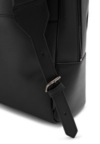 Black leather bag corner with adjustable strap and silver buckle, visible zipper, and detailed stitching on a white background.