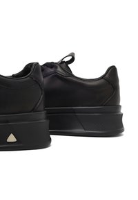 Sneaker neri con parte superiore in pelle liscia, collo imbottito, suola in gomma texture e un accento triangolare sul tallone.