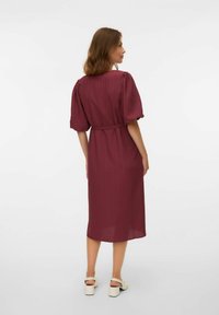 Vestido midi de textura burdeos con mangas abullonadas, cintura ceñida y silueta recta. Combinado con zapatos de tacón cuadrado en color crema.