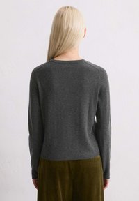 Pull gris à manches longues avec un col rond, texture tricotée et coupe légèrement cropped, associé à un pantalon en velours côtelé vert olive.