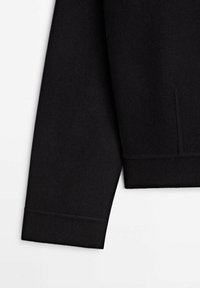 Black sweater sleeve made of textured fabric, featuring a ribbed cuff and a side seam detail. Minimalist design with clean lines.