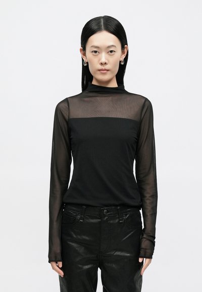 Top preto de manga comprida com tecido translúcido e texturizado nos ombros e mangas, apresentando um decote alto e um ajuste regular. Combinado com calças pretas brilhantes.