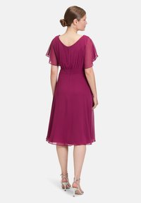 Fuchsia Kleid mit durchsichtigen Flatterärmeln, definierter Taille und knielangem Rock, ausgestattet mit einem subtilen Reißverschluss hinten und einer glatten Textur.