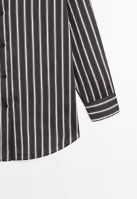 Section de chemise noire boutonnée avec de fines rayures verticales blanches et rouges et un poignet de manche longue à rayures horizontales.