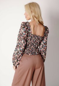 Kwiatowy crop top z bufkami, marszczonym korpusem, ciemnym tłem i pastelowymi kwiatami. Połączony z jasnobrązowymi, szerokimi spodniami o wysokim stanie.