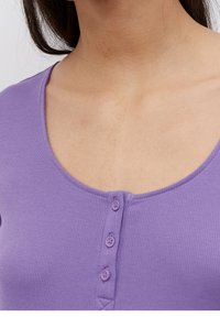 Lila, ribbade topp med rundad halsringning, prydd med fyra små knappar fram. Slät textur, avslappnad design.