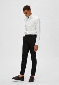 Vit skjorta med lång ärm som sitter bra, svarta skräddarsydda byxor och mörkbruna skor. Släta texturer med en klassisk design.