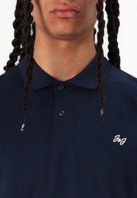 Navy blue polo shirt with three buttons and a collar; features white embroidered logo on the chest. Textured cotton material.